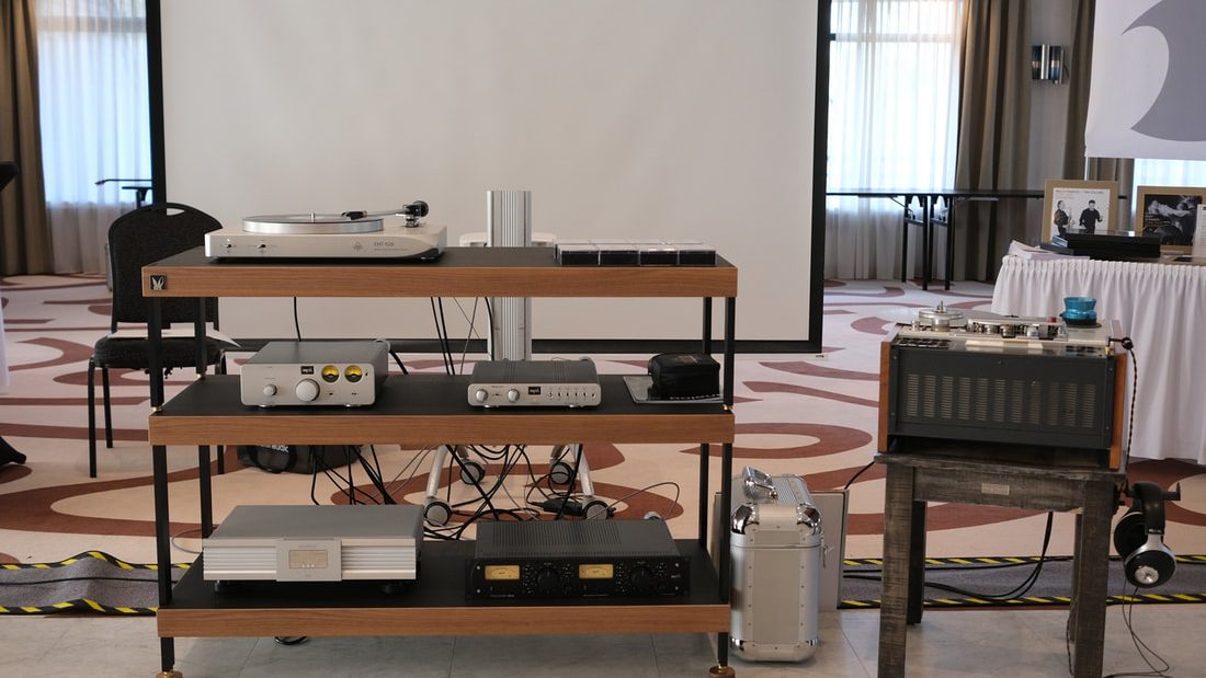 An EMT turntable and electronics on a wooden rack at a show, an older EMT broadcast turntable in its case beside it