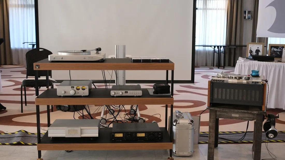 An EMT turntable and electronics on a wooden rack at a show, an older EMT broadcast turntable in its case beside it
