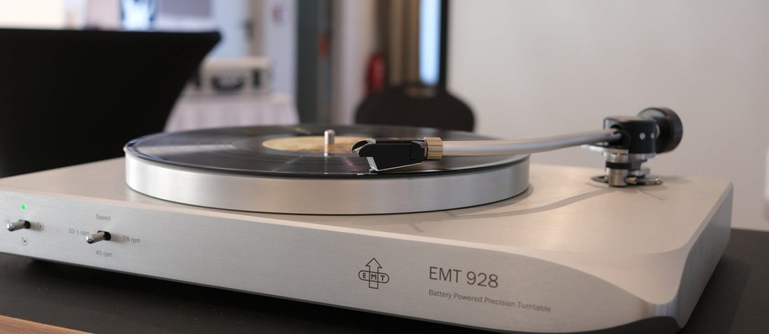 An EMT 928 turntable in silver on a wooden sideboard, a record on the platter