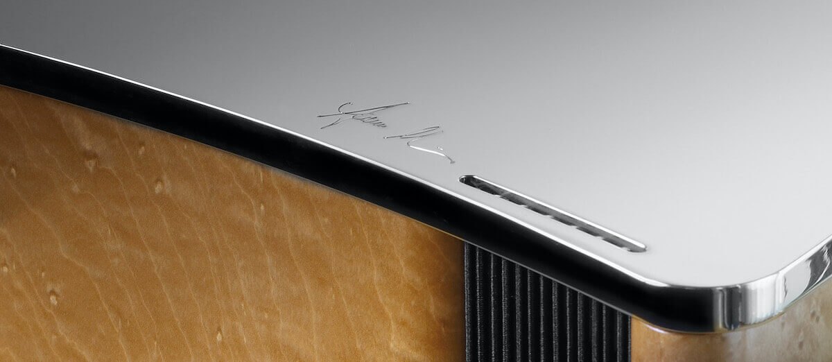 The polished aluminium top of a Ktêma loudspeaker, the founder's signature engraved in it, above a sycamore and black cabinet