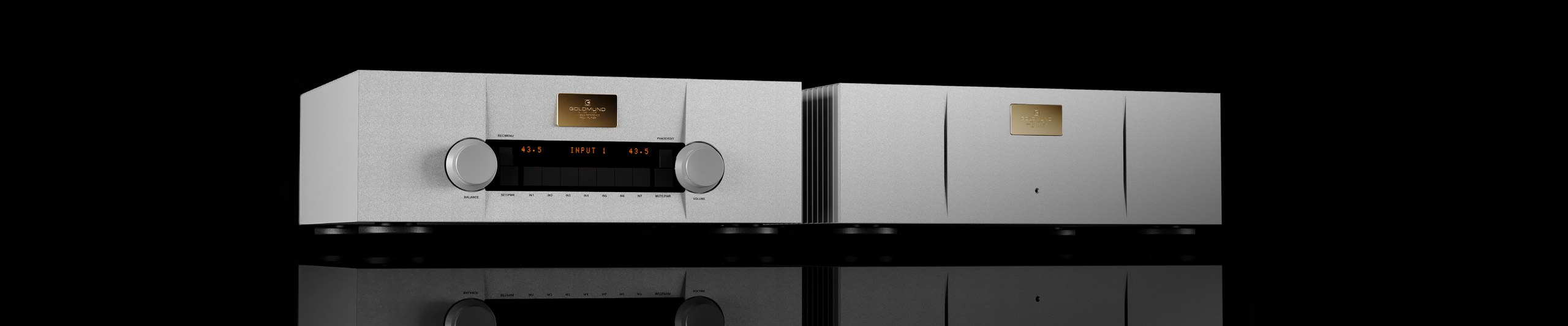 A Goldmund preamplifier and power amplifier in grey aluminium, side by side on black, mirrored in the surface beneath them