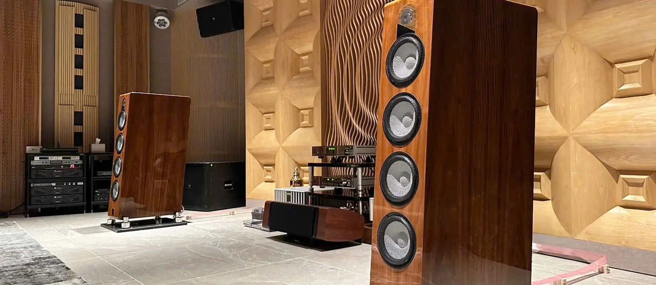 Two Marten loudspeakers in walnut, in a showroom with a sculpted wooden wall
