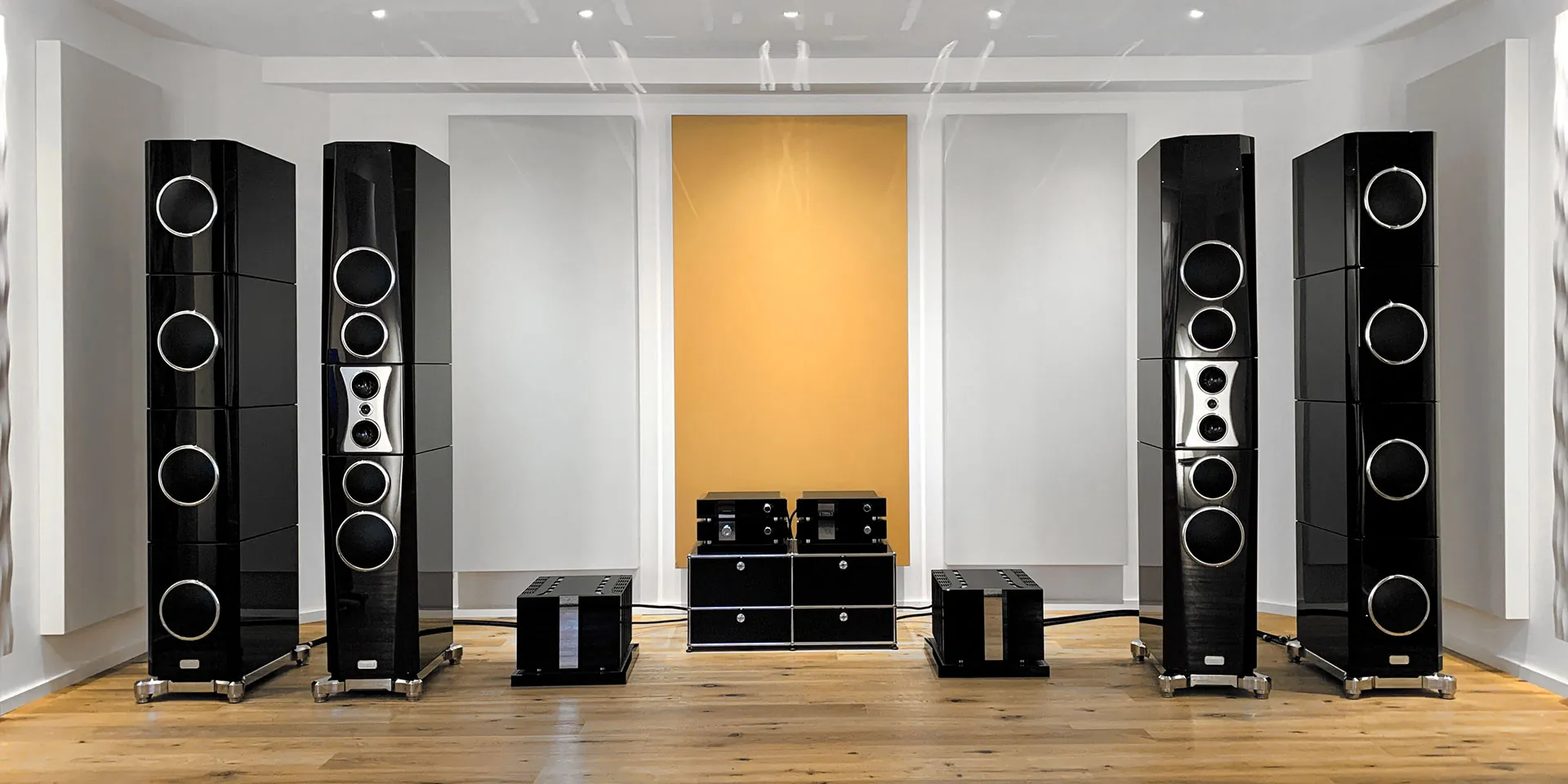Two pairs of TIDAL loudspeakers either side of their electronics, in a room with acoustic panels and a yellow panel behind the system