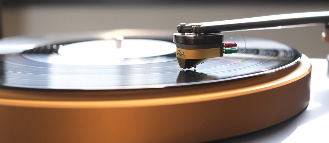 A Thales tonearm and gold cartridge on a spinning record, the copper rim of the platter in front